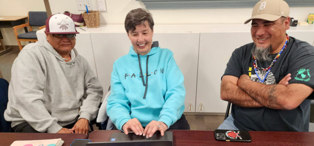 Three educators working around a laptop and smiling.