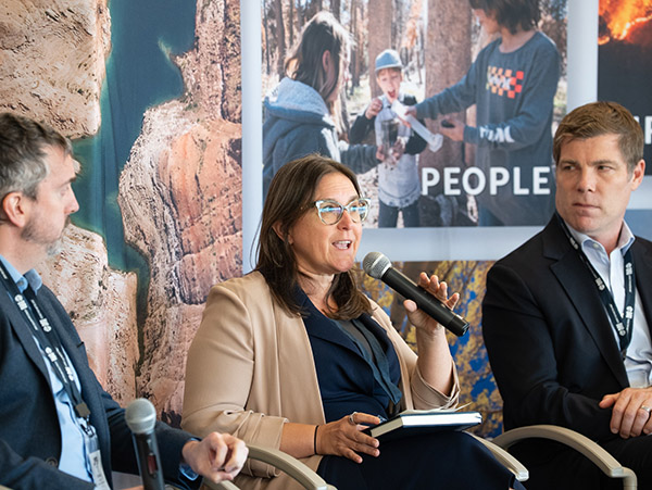 AWE 2025 2 A panelist holds the microphone in the middle of three speakers on a stage.