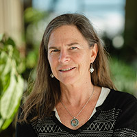 Headshot of Alison smiling in a hallway with plants wearing a dark sweater.