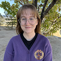 Headshot of Allison outside in front of a tree and wearing a sweater and glasses.
