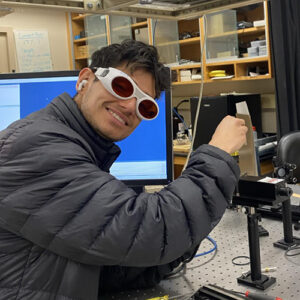 Andrew Ramirez Group Page Andrew Ramirez working in the lab and smiling for the camera while wearing safety glasses.