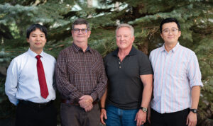 Four winners of the 2024 Celebration of Science Awards standing in a line outside in front of pine trees.