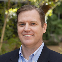 Doug Cannon smiling for the camera in a collared shirt and suit jacket. 