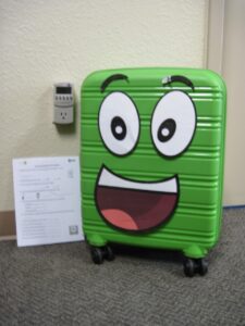 An anthropomorphic green suitcase smiles at the camera.