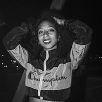 Black and white image of CoCo Jenkins wearing a Champion jacket and arms raised.