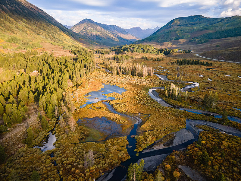 Arial image of a river running through a canyon between mountains with pine trees and scrubs.