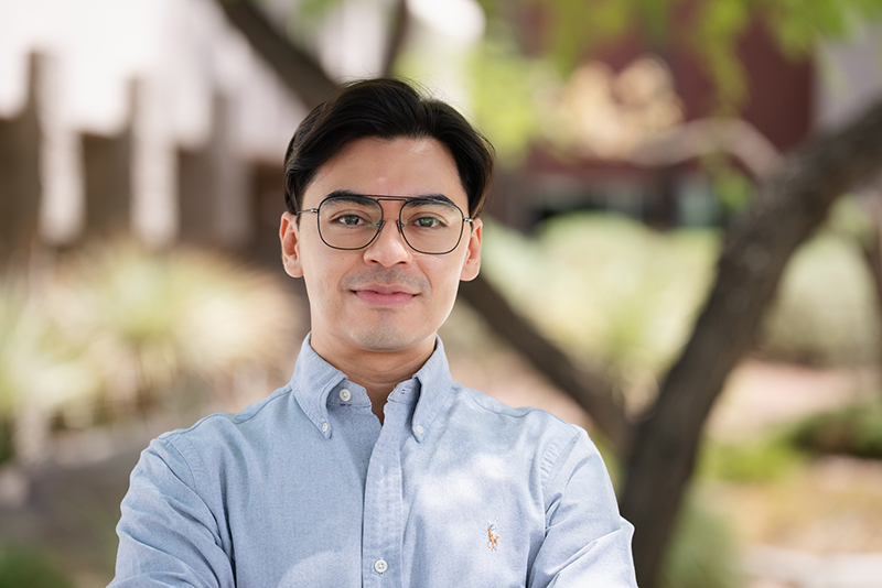 David Almanza standing outside in front of a tree in a light blue collared shirt and wearing glasses.