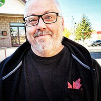 Selfie image of Dickenfella outside in the sun wearing glasses and a jacket. 