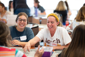 Nevada educators smiling and laughing while programming small robots on a track on a tabletop.