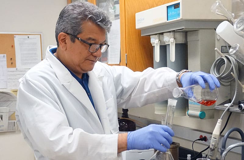 male Hispanic scientist work in lab pouring water into a test tube