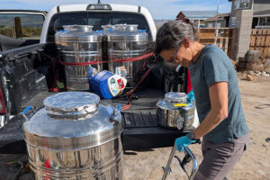 Scientist with a large water container on a dolly in front of a pickup truck.