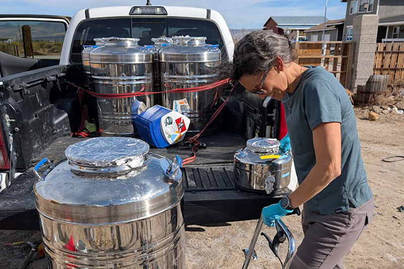 Scientist with a large water container on a dolly in front of a pickup truck.