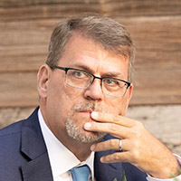 Headshot of Geoff wearing a suit and glasses looking just off camera. 