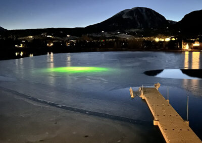 A green light is glowing under the surface of a frozen lake.