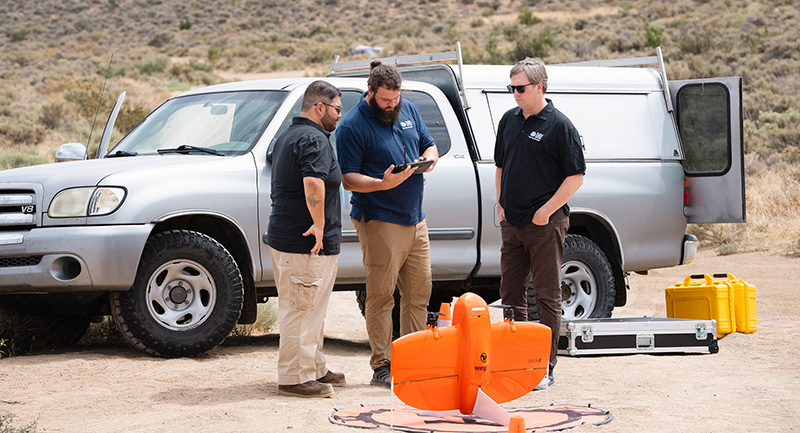 ITAP Our Impact Page Three researchers wearing DRI shirts out in the desert landscape looking at a tablet with a drone in front of them.