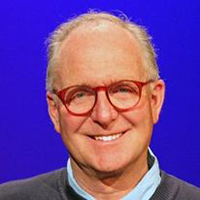 Headshot of John against a blue background and wearing red glasses.