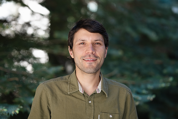 Juan Henao smiling at the camera in front of trees in a green shirt.