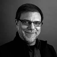 Black and white headshot of Julian Kilker wearing glasses against a neutral background. 
