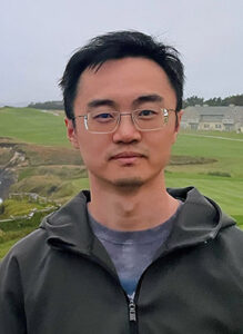 Photo of Kailong Li outside along a coastline wearing a hoodie and glasses.