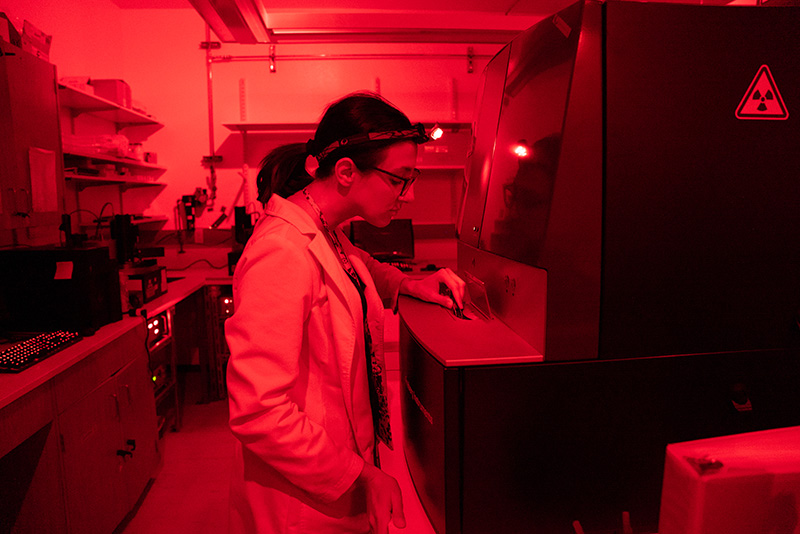 A researcher works with a piece of large equipment in a lab with a red glow. 