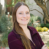Headshot of Megan smiling with arms folded in front of a desert landscape. 