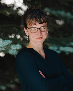 Headshot of Meghan Collins outside in front of pine trees. 