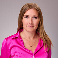 Headshot of Monnette smiling and wearing a pink button down shirt against a neutral background. 