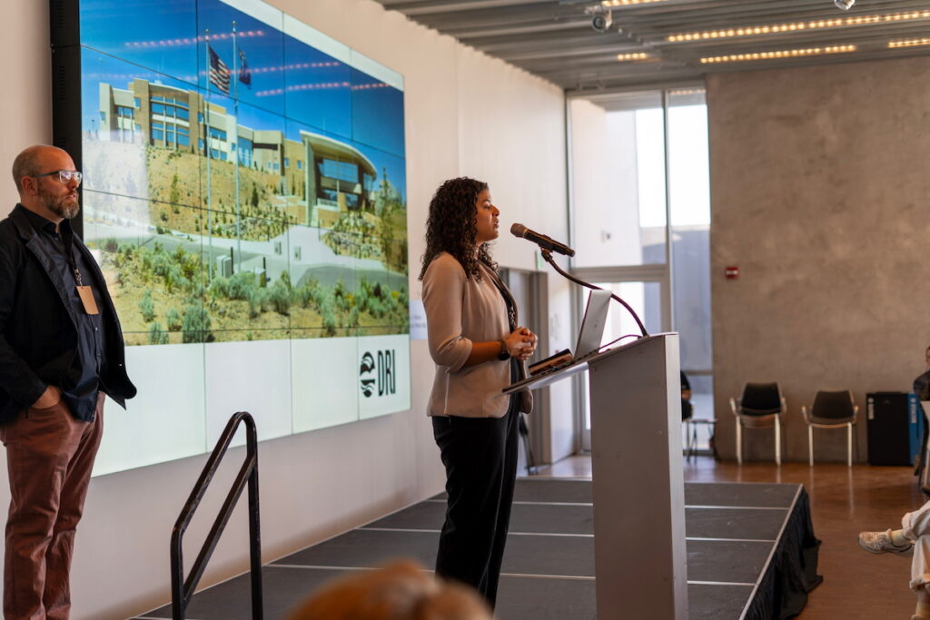 Woman standing on a stage speaking at a podium. 