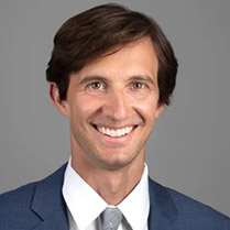 Headshot of Nicholas Nassikas wearing a dark grey suit against a neutral background. 