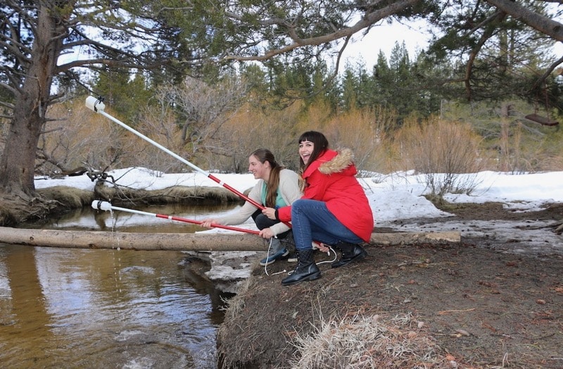 two female scientists collect water samples from lake