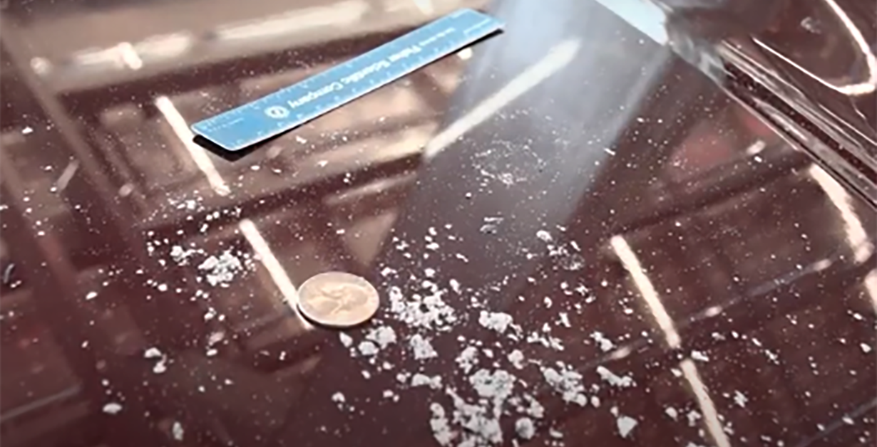 Ash on the hood of car with a ruler and quarter to indicate the size of the ash.