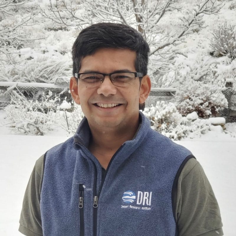 DRI Scientist smiles as he stands in front of snowy trees and backdrop