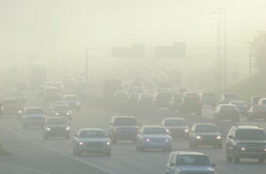 Thick smog hovers over a highway during rush hour traffic.