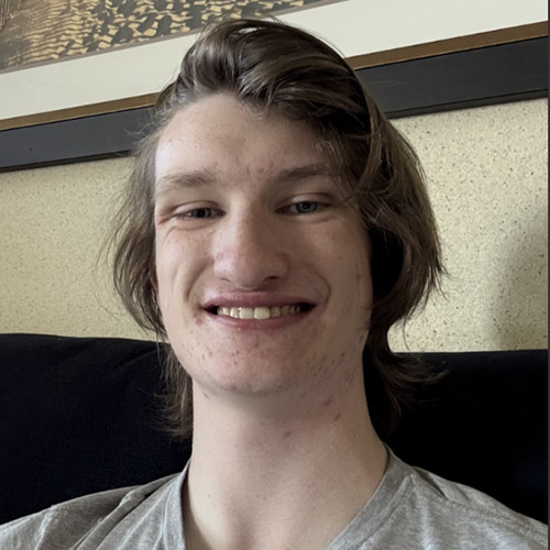 Russell N Christensen Group Page Headshot of Russell smiling at the camera with a yellow wall and framed picture in the background.