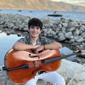 A boy sitting on a rock holding a cello
