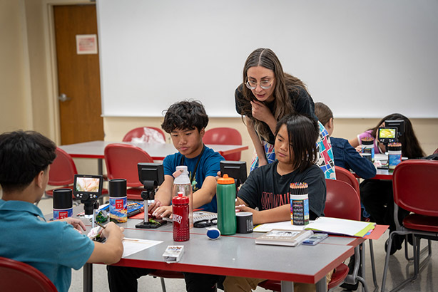 An instructor is helping two students at a table with a STEM activity.