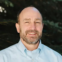 Headshot of Sean McKenna in a blue collared shirt and pine trees in the background.