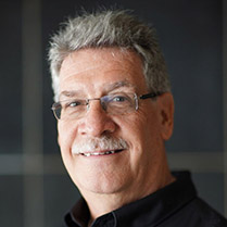 Headshot of David Shew smiling and wearing glasses against a neutral dark background.