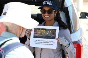 Tiffany is wearing a DRI hat and holding up a picture of the Las Vegas Bearpoppy to a group of volunteers.