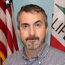 Tony Marino Headshot against a blue background with the American Flag. 