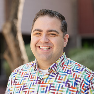 Headshot of Trevor outside and smiling wearing a colorful button down shirt. 