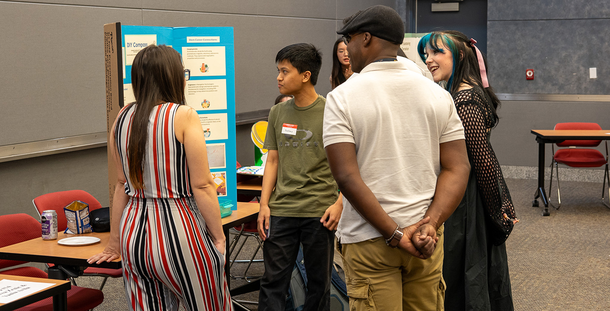 Students gathered around a presenter with a poster presentation. 