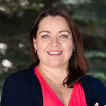 Headshot of Vera Samburova outside in front of pine trees smiling with arms crossed.