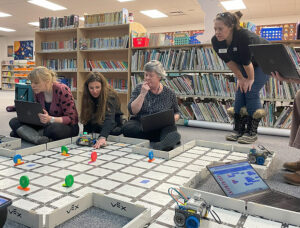 Four women looking at a robot in a classroom.