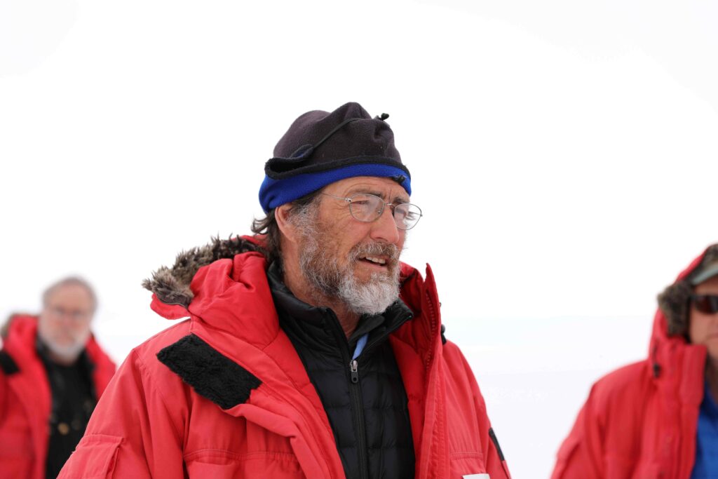 Researcher wearing red coat, hat and glasses against a snowy landscape with two others. 