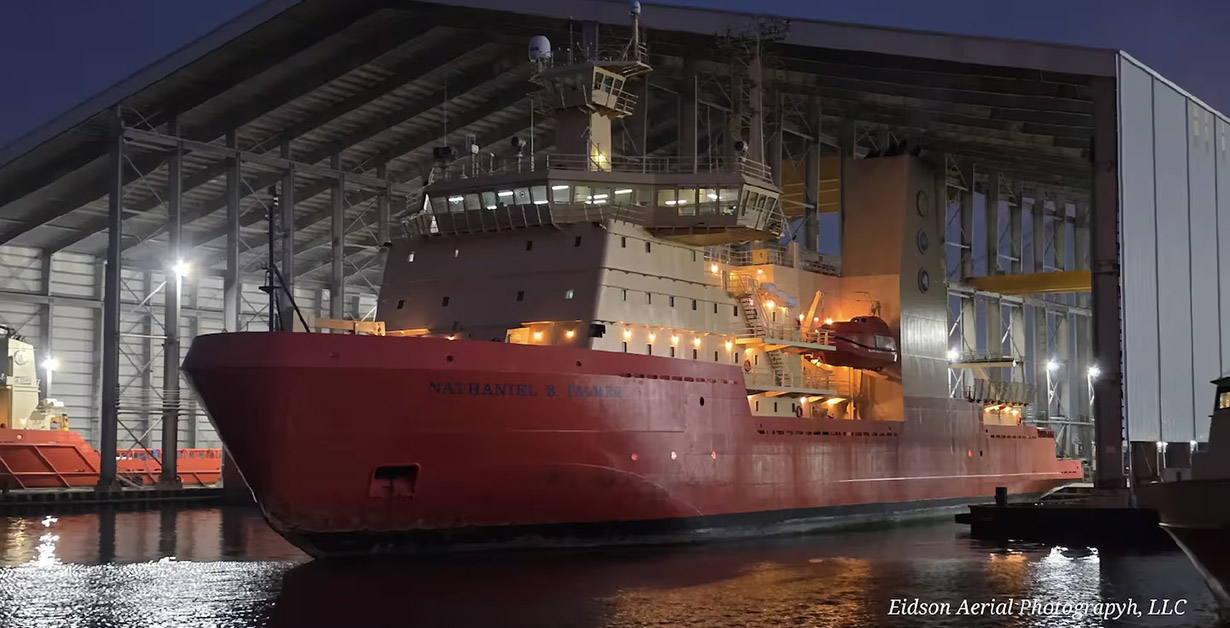 A large ship with a red hull in a covered dock.