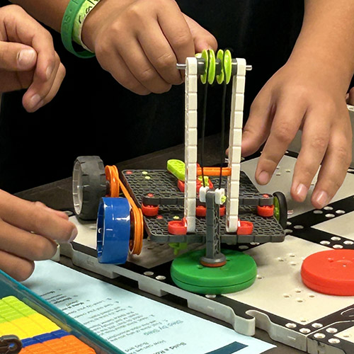 Closeup of student hands working on putting together a robot. 