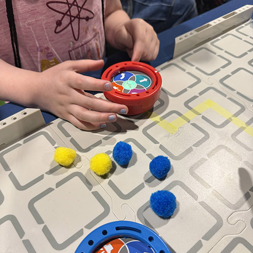 Close up of a grid table and a student working with a small puck style robot. 